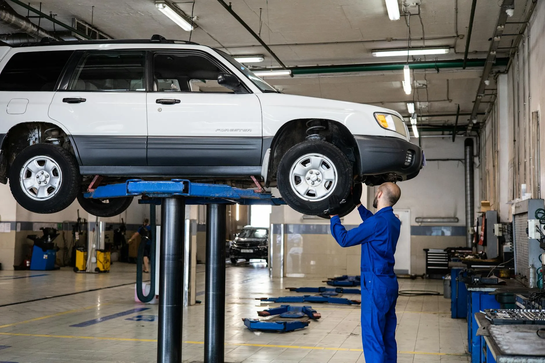 Mechanik ogląda białą Skodę w podniesionym aucie w warsztacie