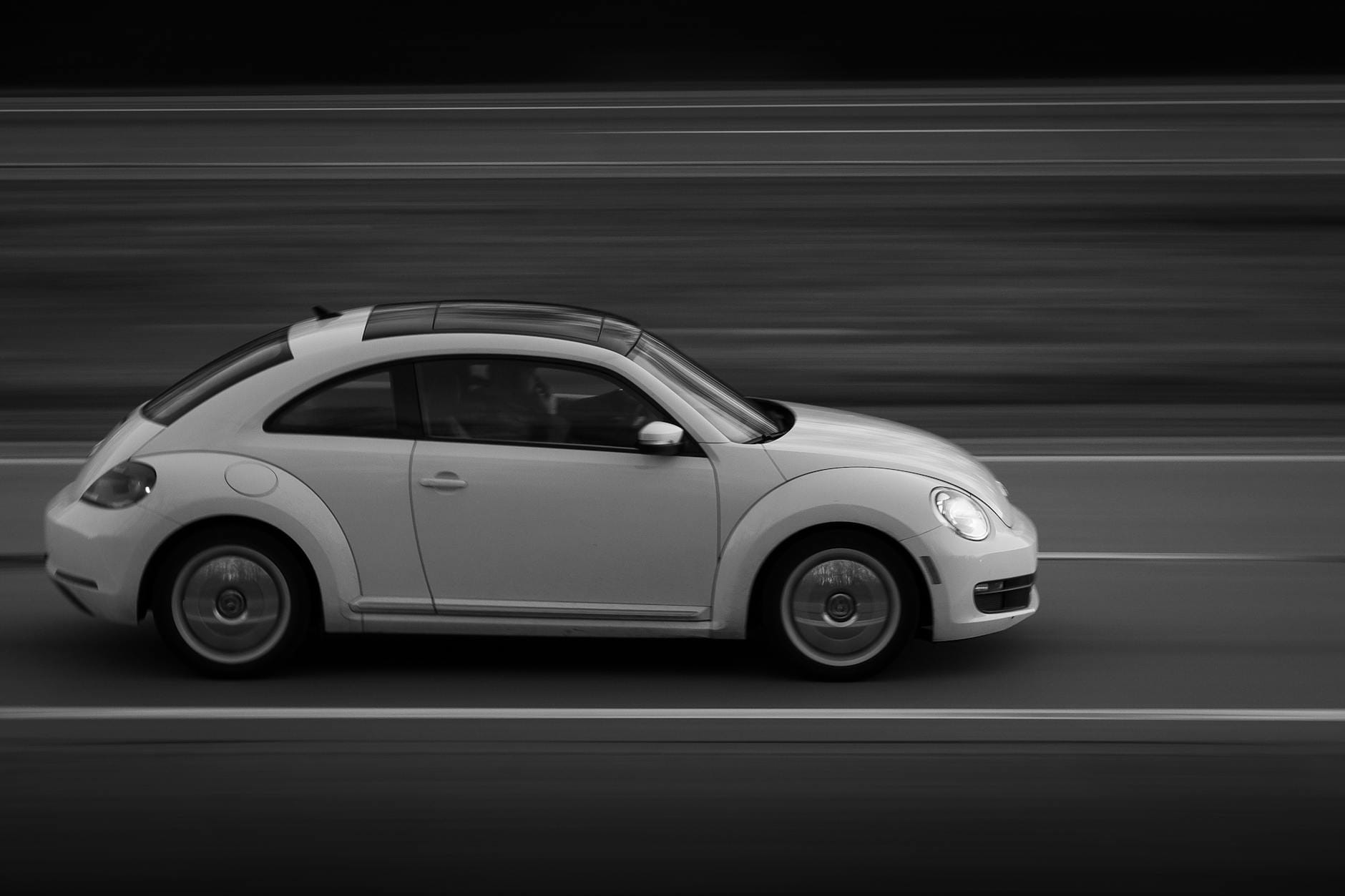 Volkswagen Beetle pędzący drogą w czarno-białym ujęciu z boku