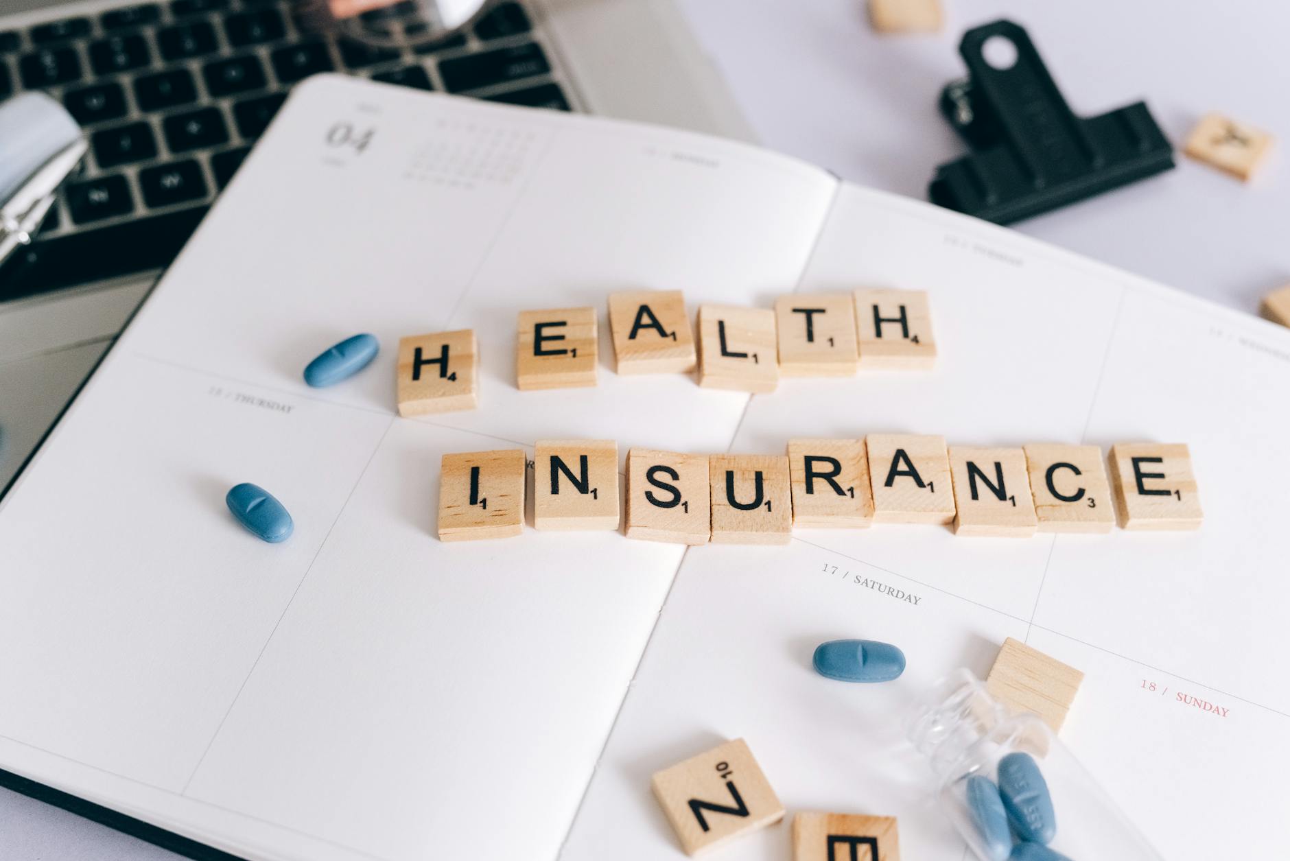 Kostki scrabble health insurance na planerze obok tabletek i laptopa