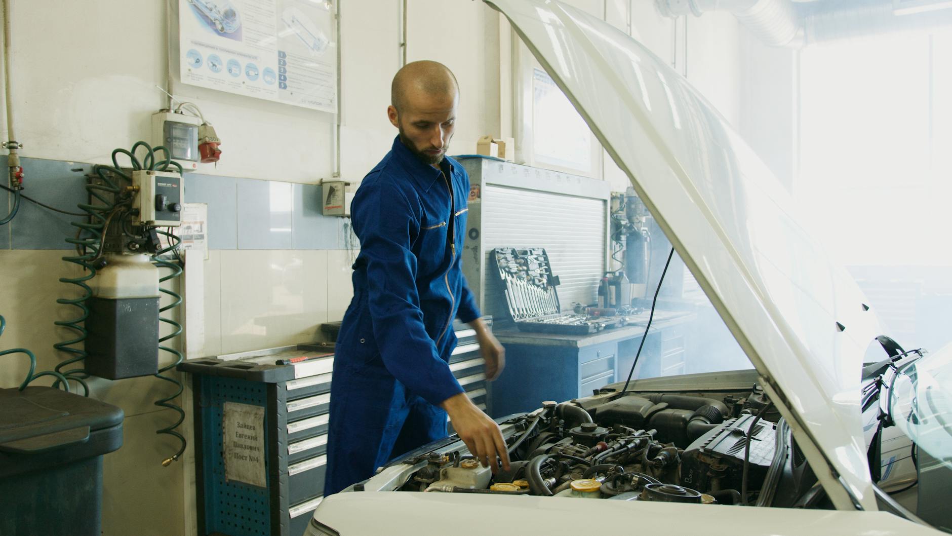 Mechanik w niebieskim kombinezonie sprawdza silnik BMW w warsztacie