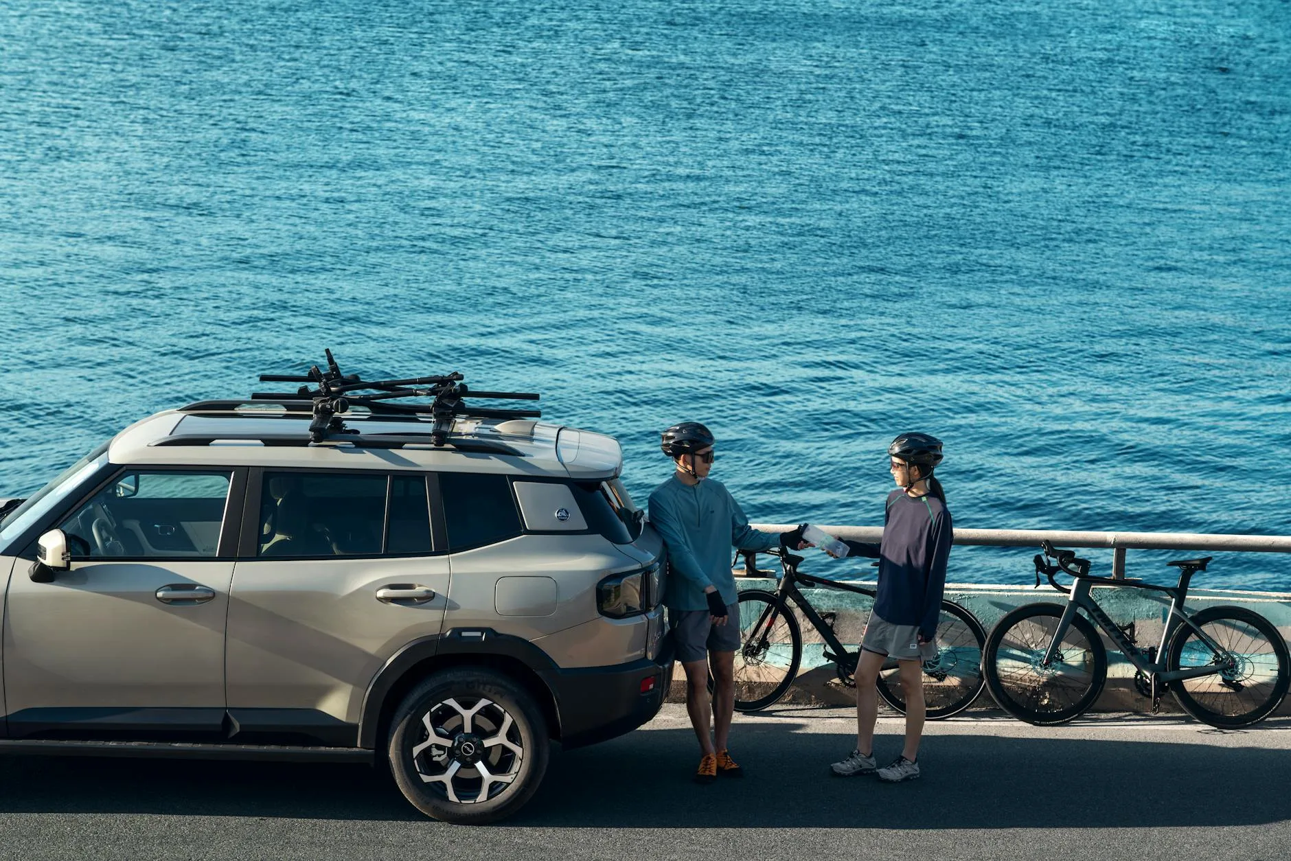 SuV Volvo załadowany sprzętem przy oceanie, obok stoją rowerzyści