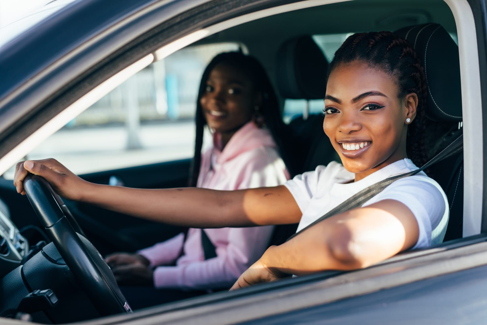 Perfect start of holidays. Two beautiful african young cheerful women looking at each other with smile while sitting in car