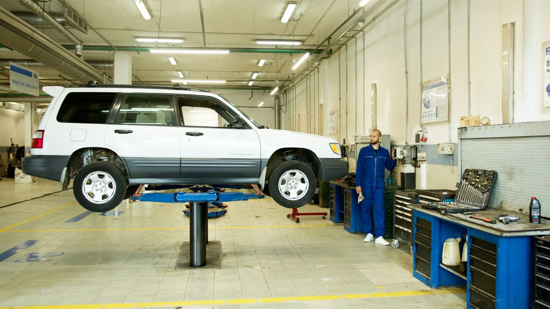 Mechanik w niebieskim kombinezonie przy Subaru Outback na podnośniku