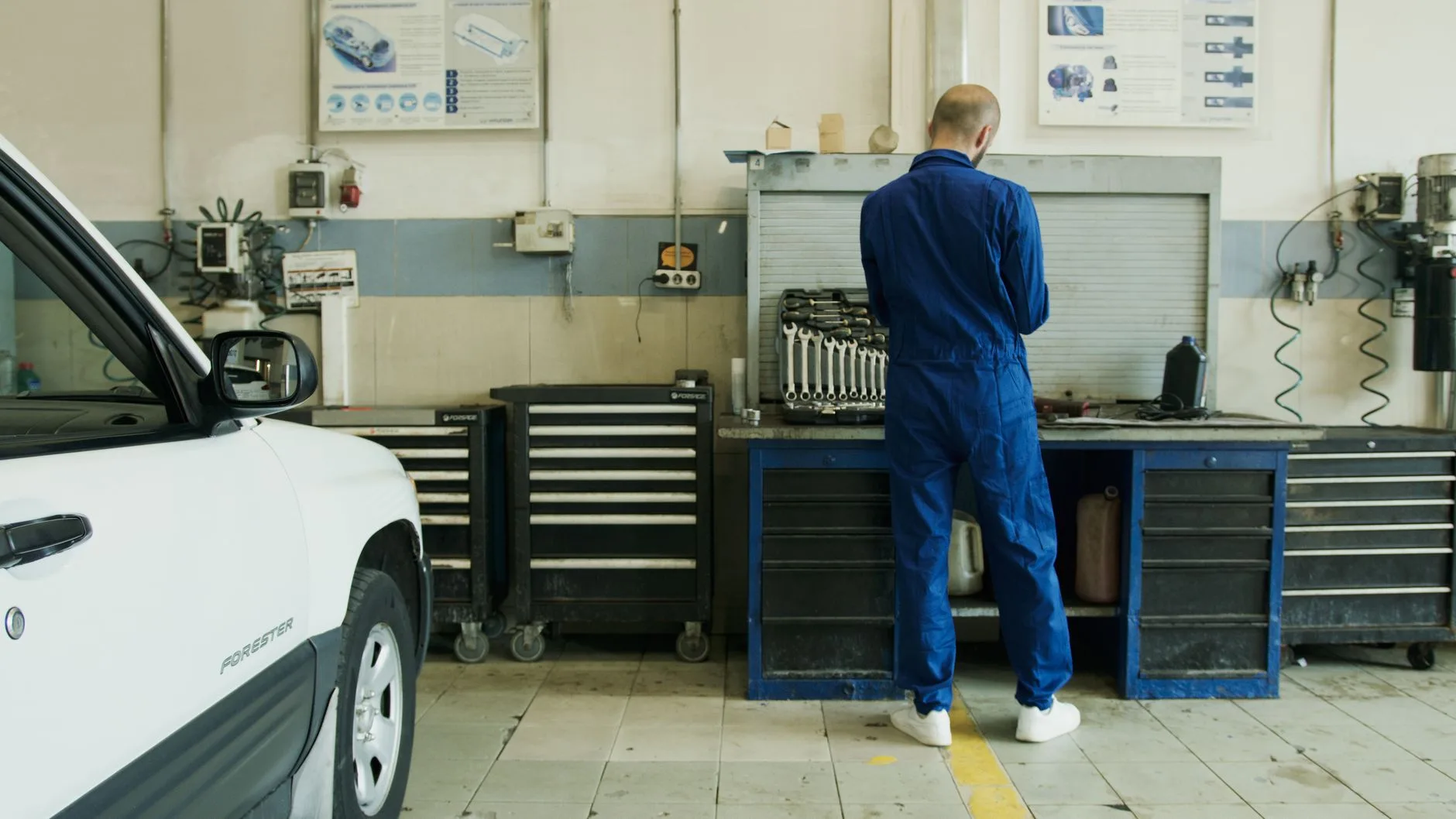 Mechanik w niebieskim kombinezonie sprawdza białe Subaru w garażu